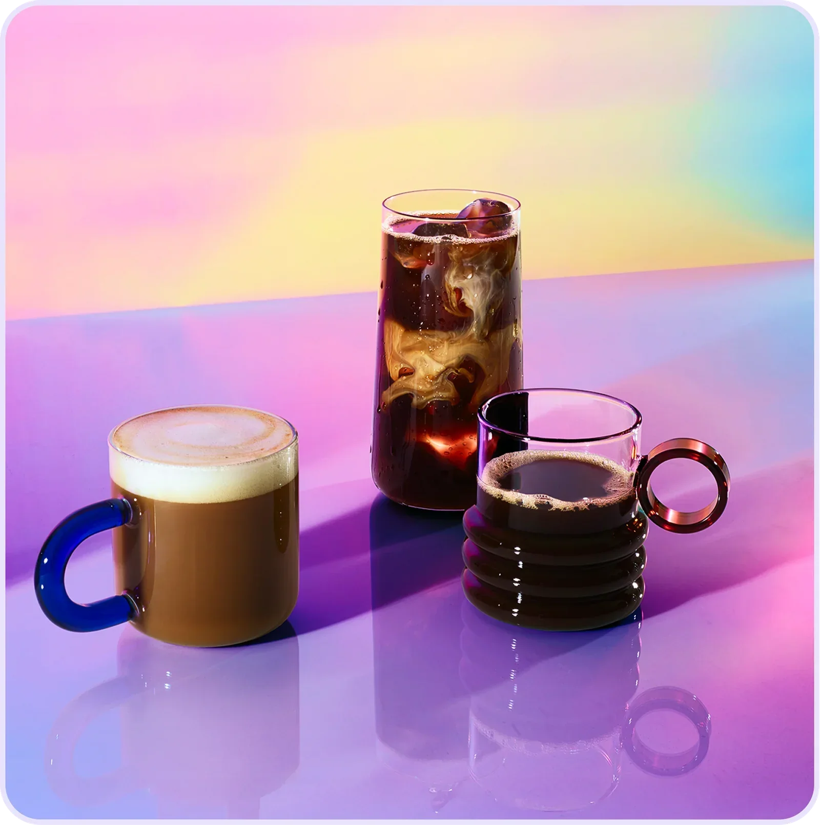 Three coffee drinks displayed on a reflective surface against a colorful pastel background