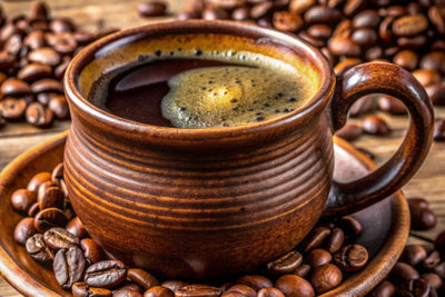 Steaming cup of black coffee in a brown ceramic mug surrounded by roasted coffee beans on a wooden table