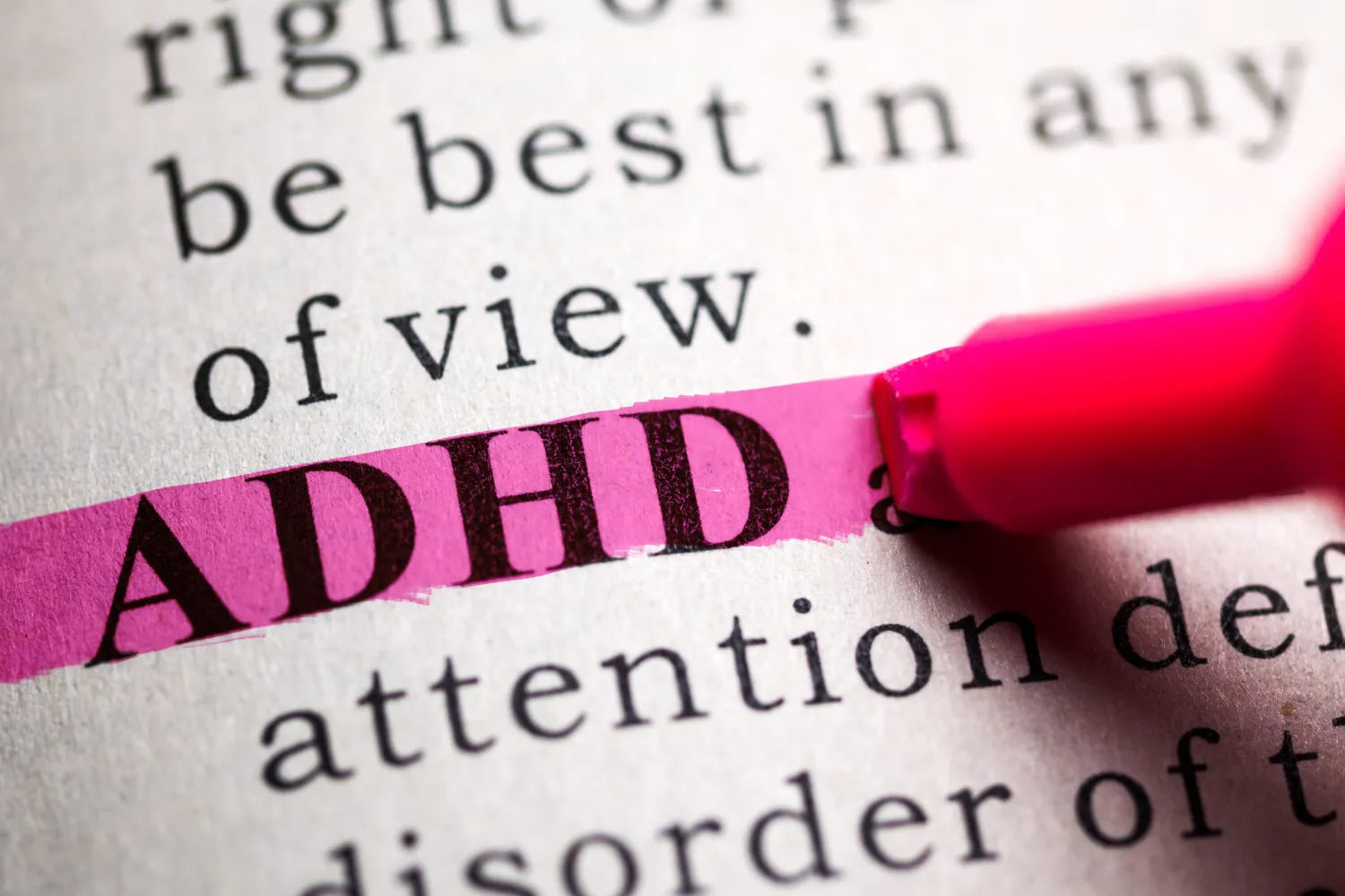 Close-up of the word ADHD highlighted in pink with a pink highlighter on a printed page