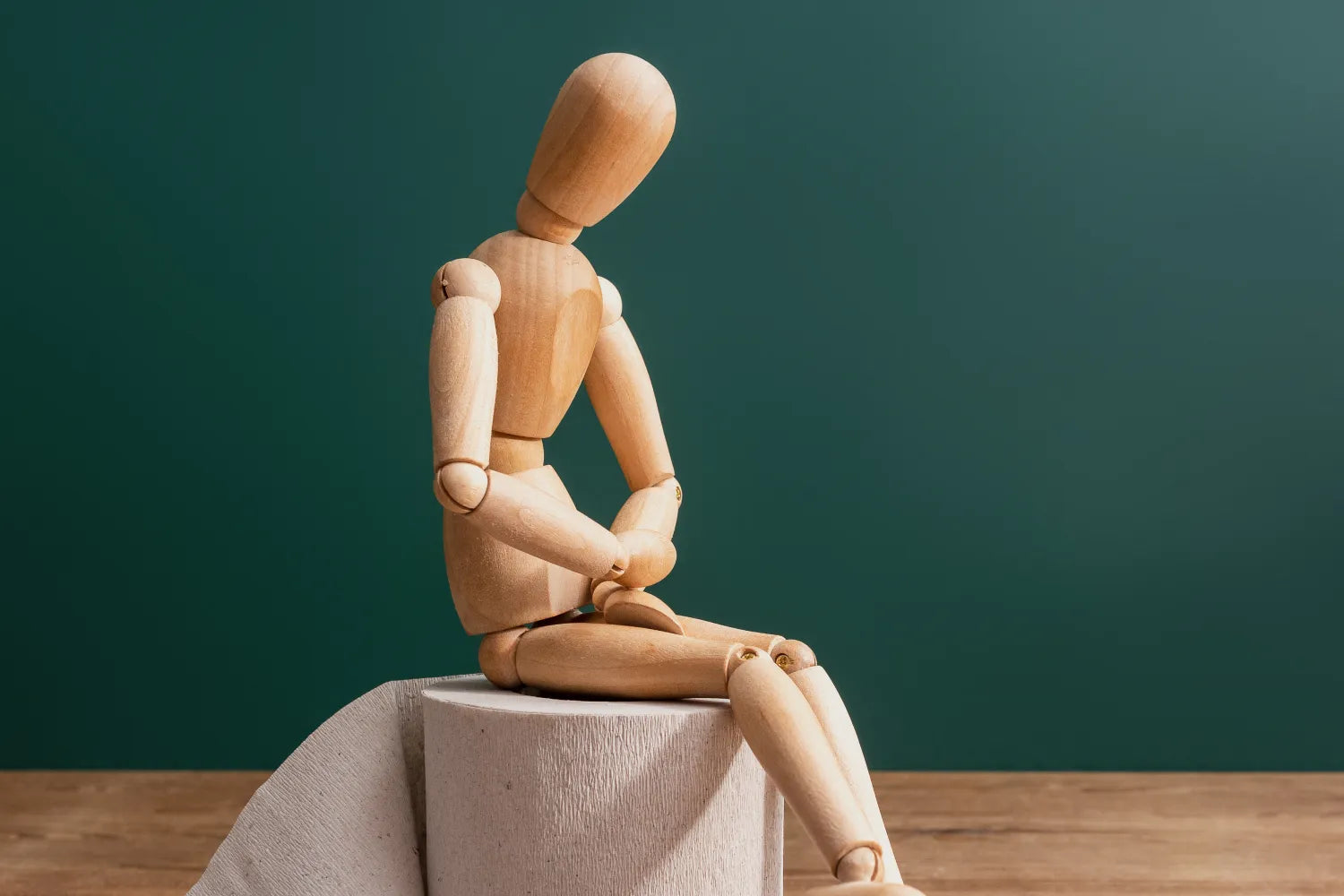 Wooden mannequin sitting and clutching its abdomen against a green background, representing stomach discomfort