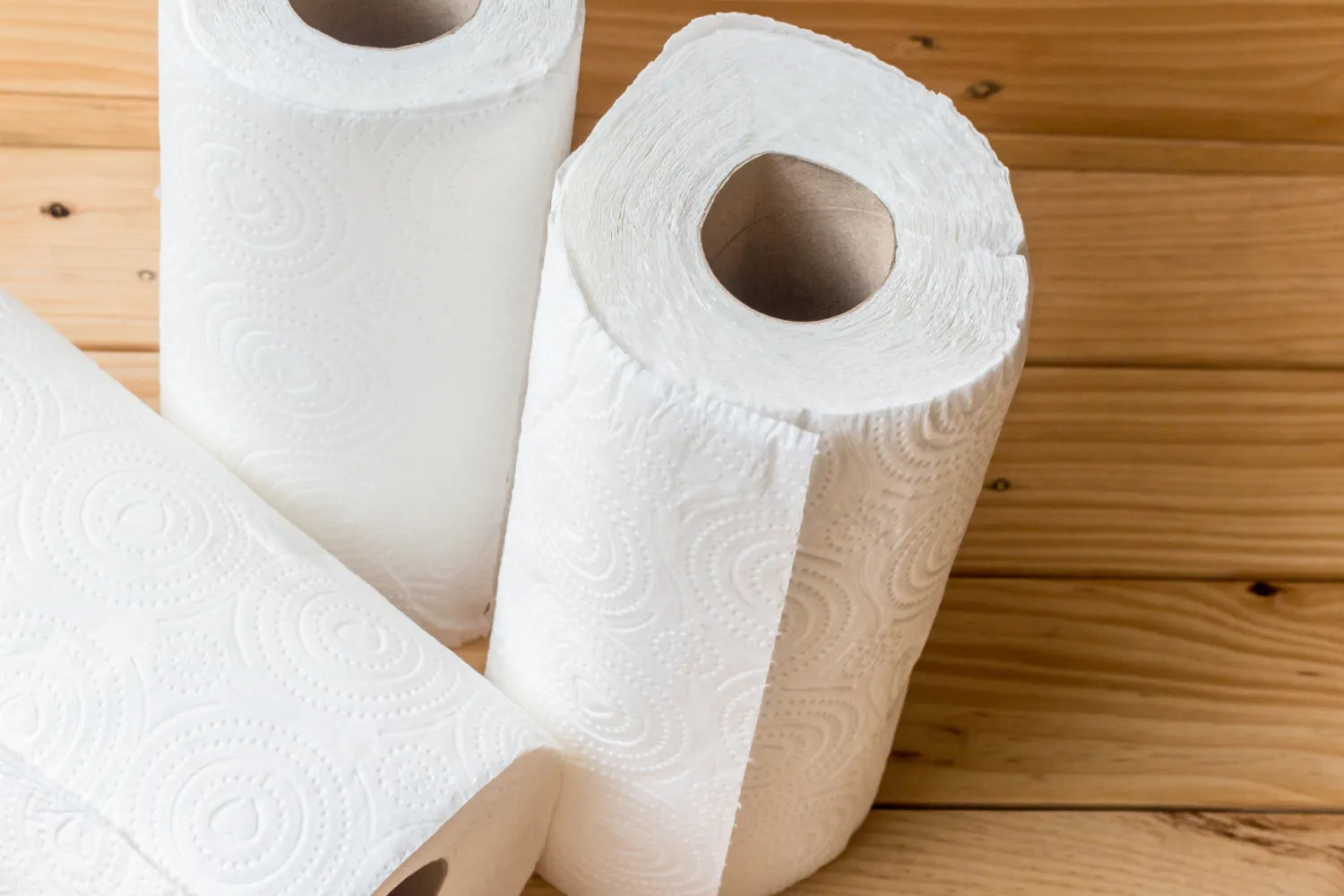 Top-down view of three white paper towel rolls showing embossed quilted texture on a wooden table