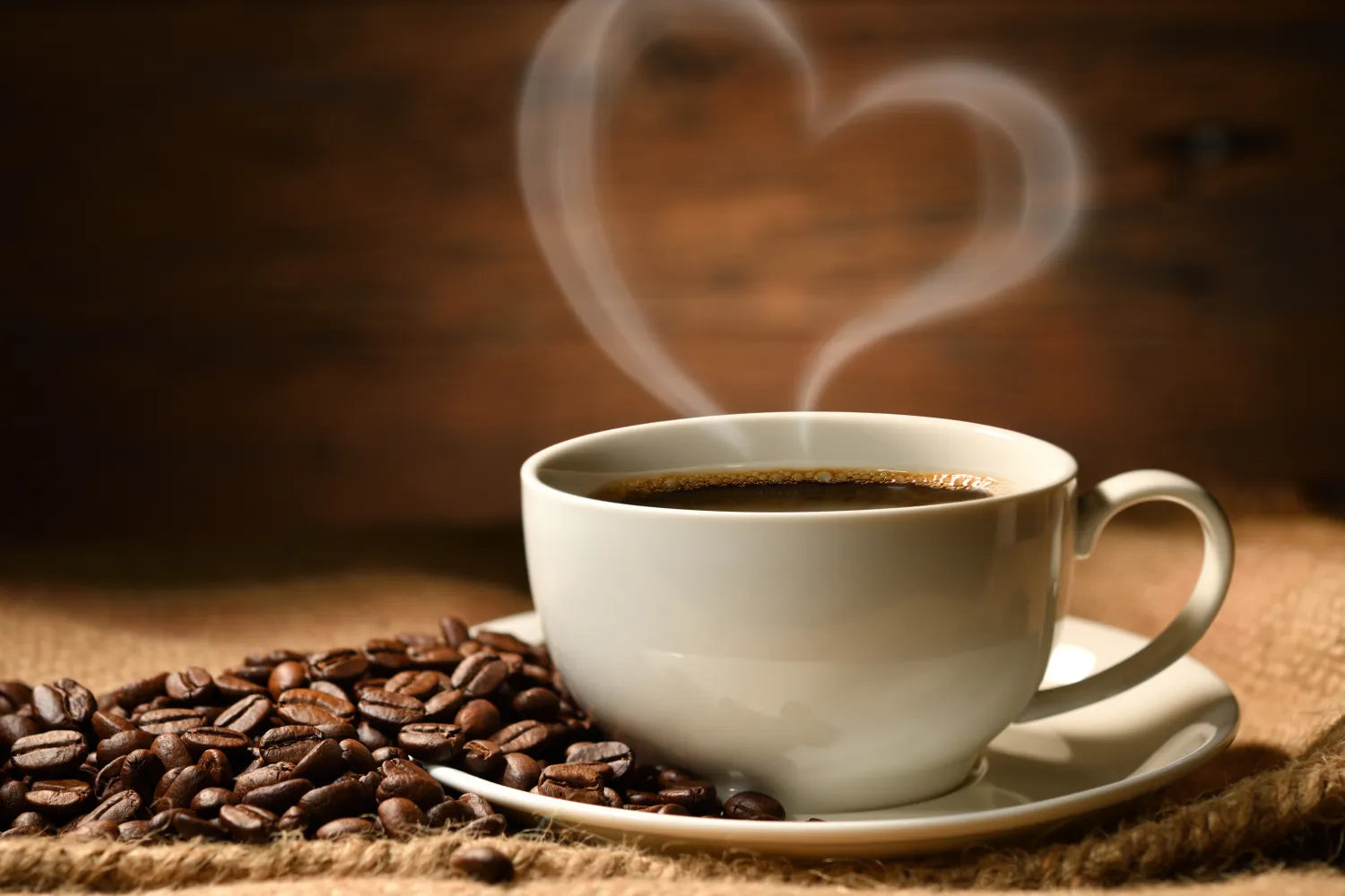 Steaming cup of coffee with heart-shaped steam and roasted coffee beans on a burlap surface