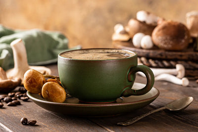 Green ceramic cup of mushroom coffee on saucer with fresh mushrooms and coffee beans on a rustic wooden table