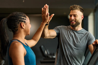 Woman and man high-fiving on treadmills in a gym, smiling after a workout