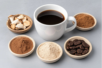 Cup of black coffee surrounded by small bowls of mushroom pieces, mushroom coffee powders, and roasted coffee beans on a gray surface