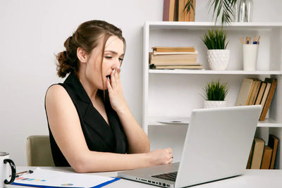 Woman yawning at a desk in front of a laptop in a bright home office