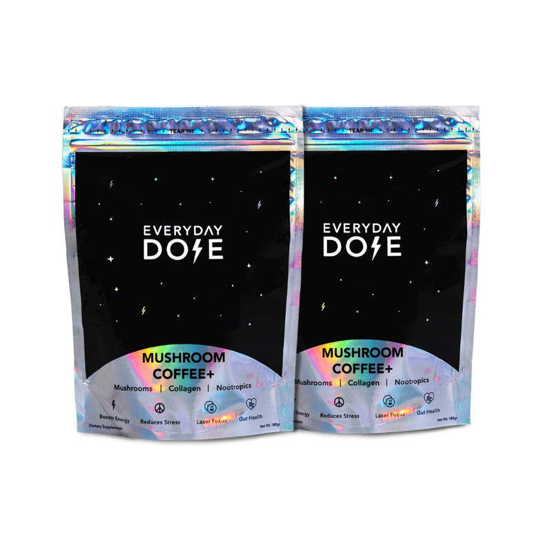 Two black holographic packages of 60-Servings Everyday Dose Mushroom Coffee Plus with iridescent trim and starry design