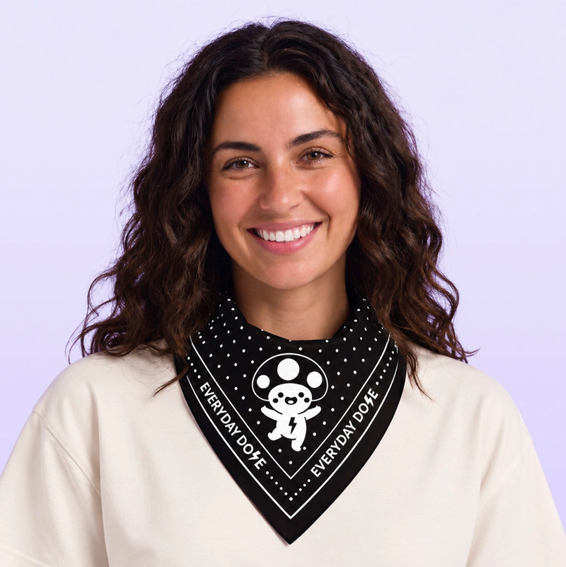 Smiling woman wearing a black patterned bandana with white lettering and a cartoon graphic over a cream top against a lavender background