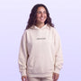 Smiling woman wearing a light pink hooded sweatshirt with small chest lettering against a soft lavender background