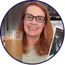 Smiling woman with red hair and glasses holding a glass of iced coffee in a bright indoor setting