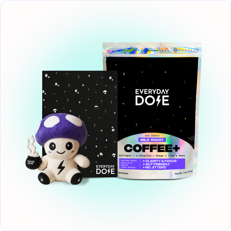 Plush mushroom toy holding coffee cup beside black notebook and bag of Everyday Dose mild roast coffee blend